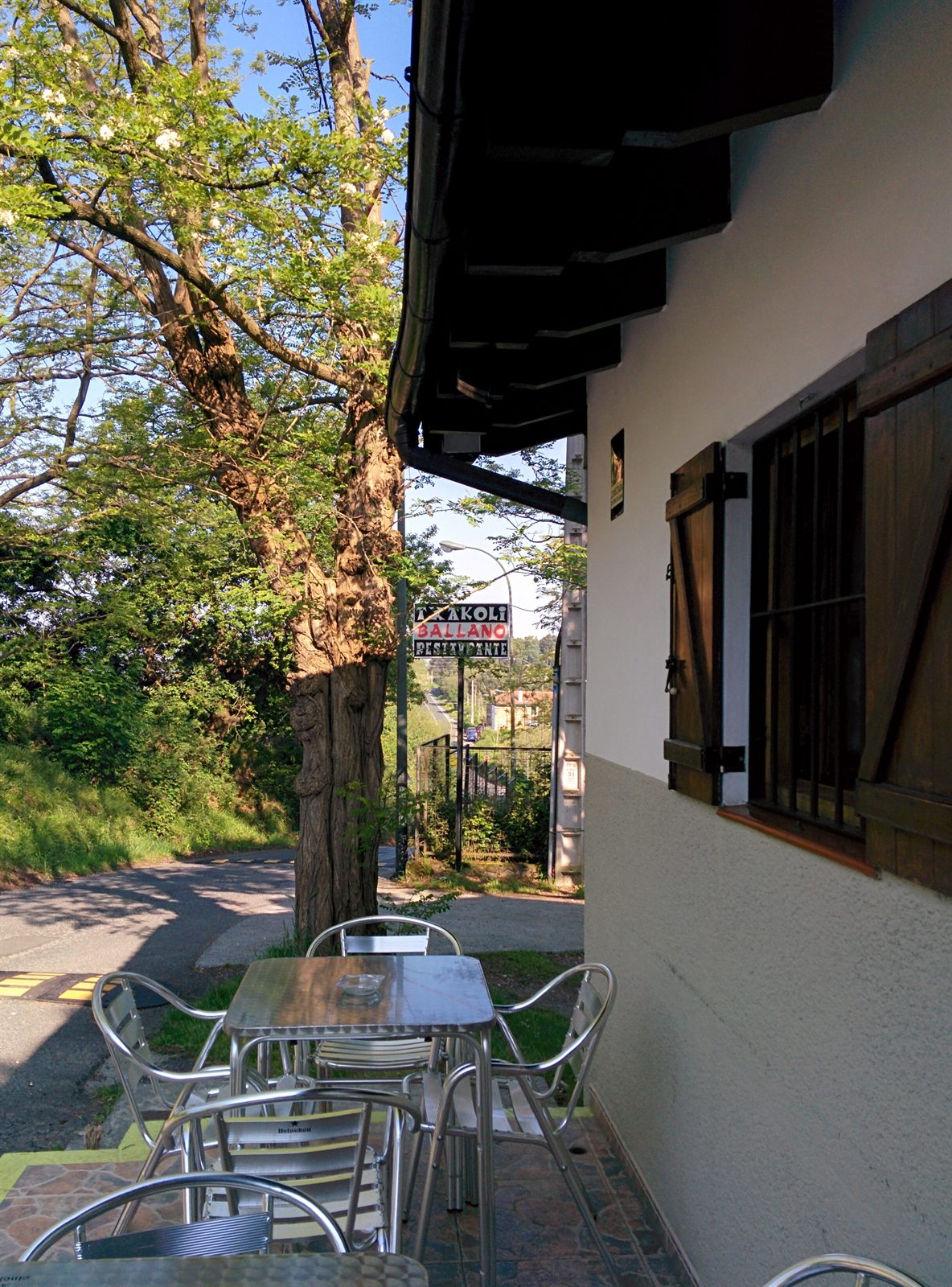 Terraza exterior de Txakoli Ballano entre árboles, con la carretera de Artxanda al fondo